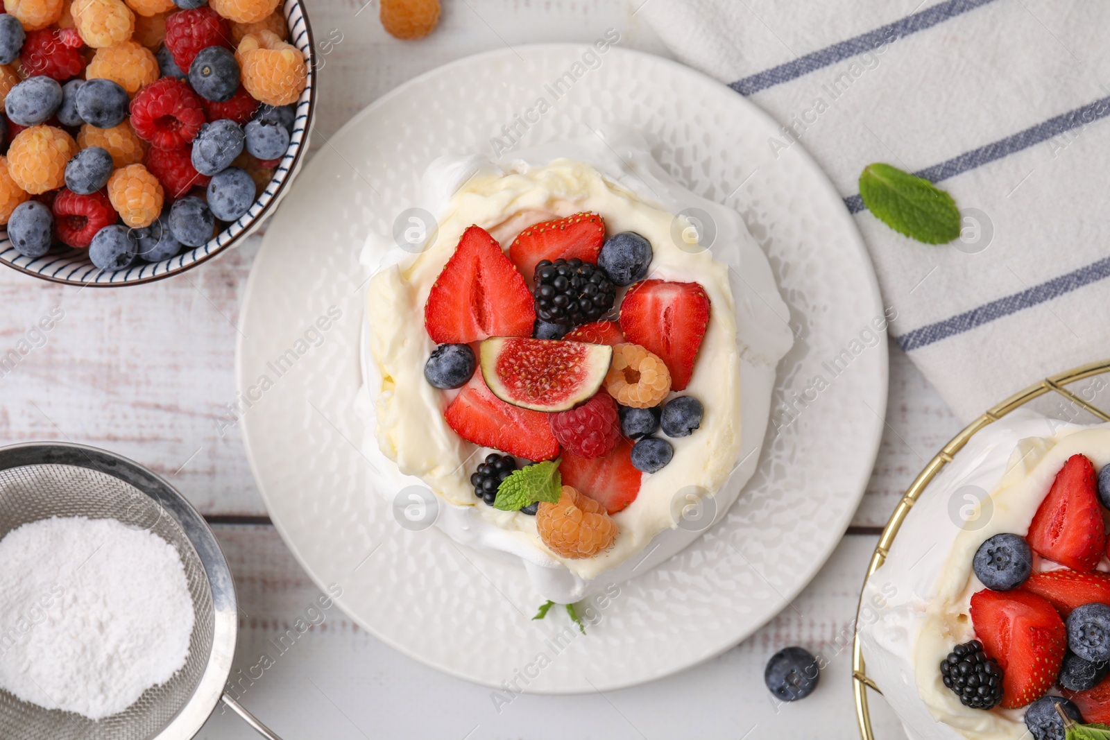 Photo of Pavlova cake (meringue dessert) with whipped cream, fresh berries, fig and mint on white wooden table, flat lay