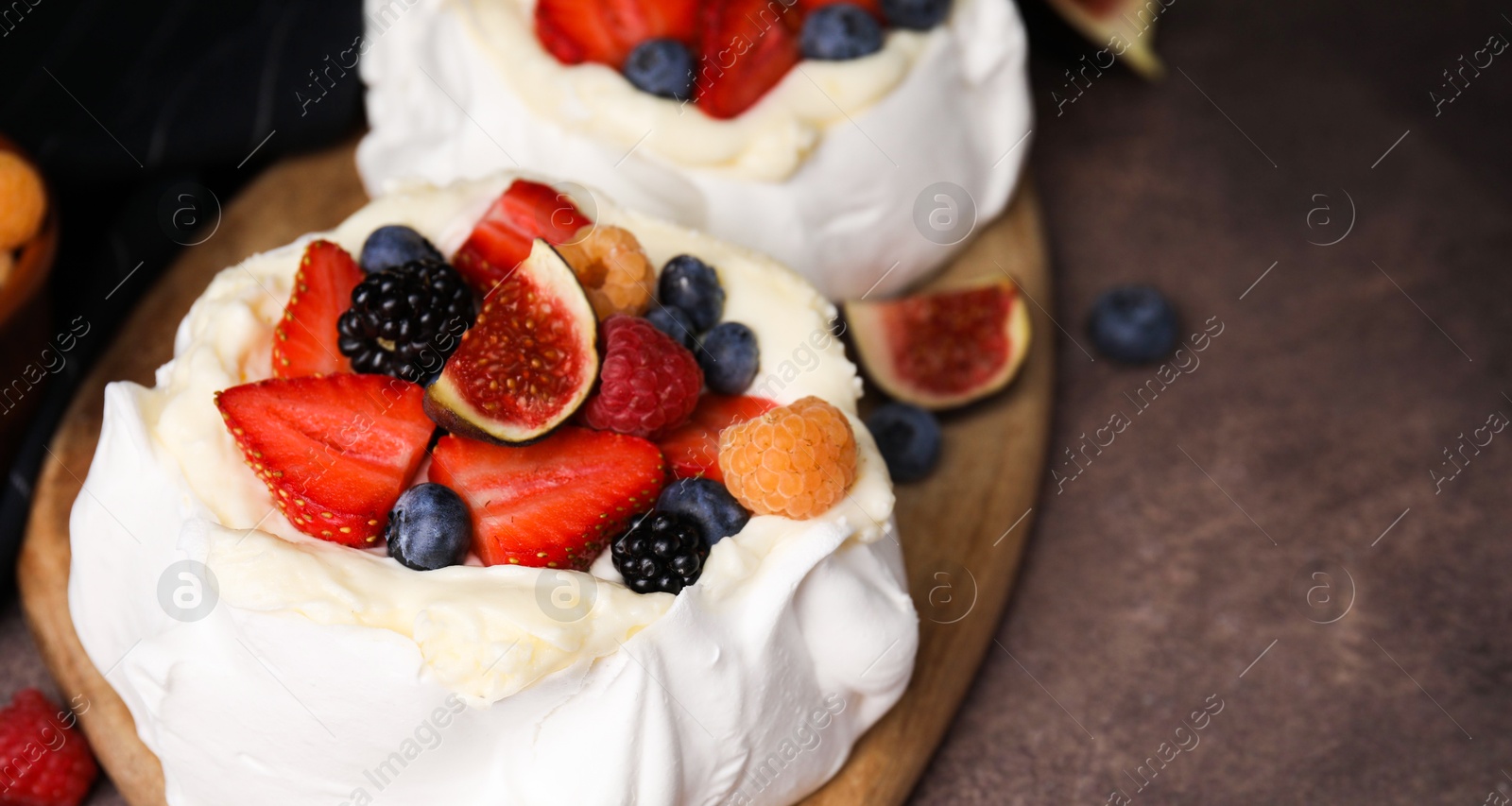 Photo of Pavlova cake (meringue dessert) with whipped cream, fresh berries and fig on brown table, closeup. Space for text