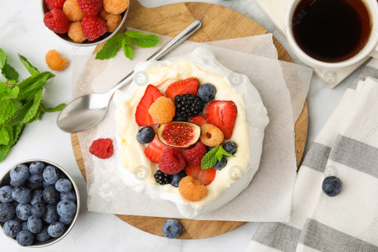 Photo of Pavlova cake (meringue dessert) with whipped cream, fresh berries, fig and mint on white marble table, flat lay