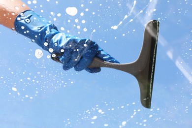 Photo of Woman washing window with squeegee tool against blue sky, closeup