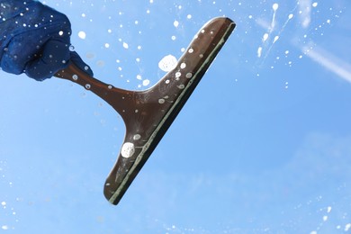 Photo of Woman washing window with squeegee tool against blue sky, closeup