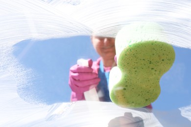 Photo of Woman washing window with sponge against blue sky, closeup