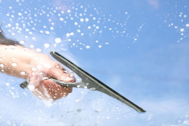 Photo of Woman washing window with squeegee tool against blue sky, closeup