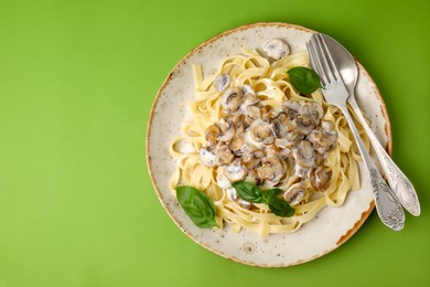 Photo of Delicious pasta with mushrooms and basil served on light green background, top view. Space for text