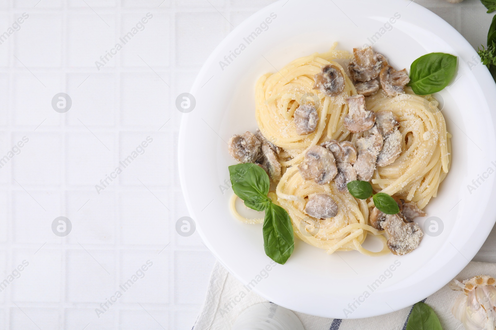 Photo of Delicious pasta with mushrooms and basil on white tiled table, top view. Space for text