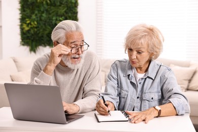 Pension savings. Senior couple planning budget at white table indoors