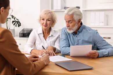 Photo of Pension plan. Senior couple consulting with insurance agent at wooden table indoors