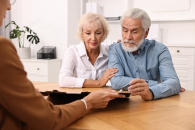 Photo of Pension plan. Senior couple consulting with insurance agent at wooden table indoors