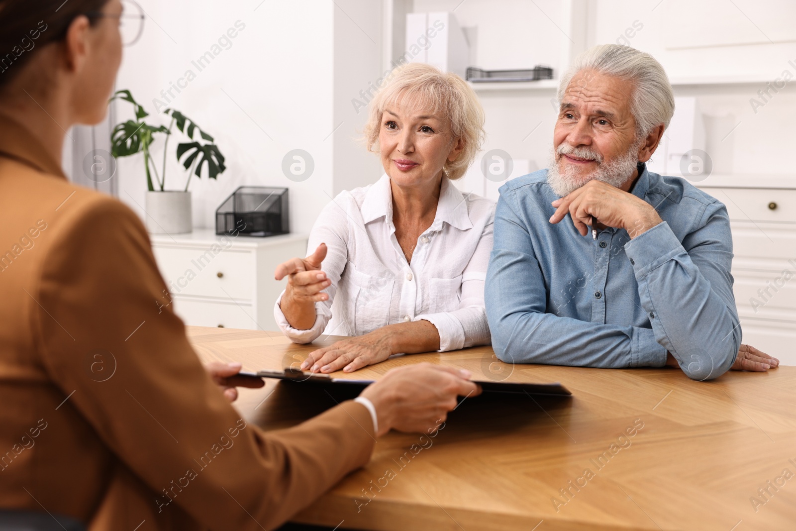 Photo of Pension plan. Senior couple consulting with insurance agent at wooden table indoors