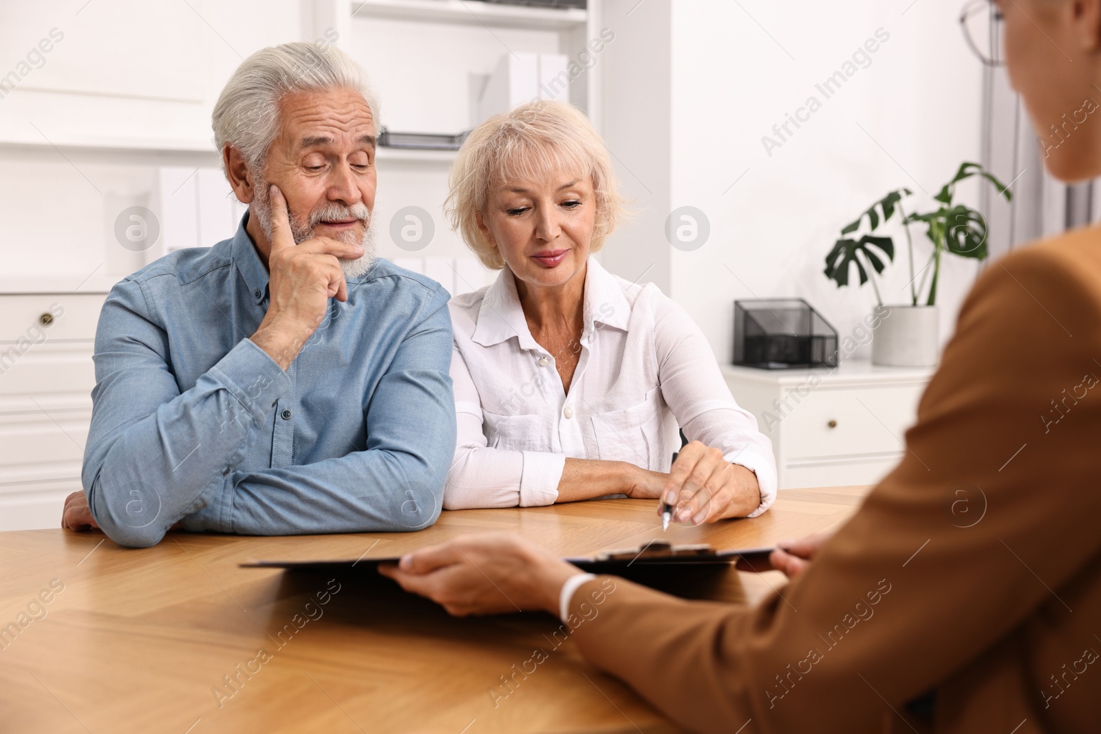 Photo of Pension plan. Senior couple consulting with insurance agent at wooden table indoors