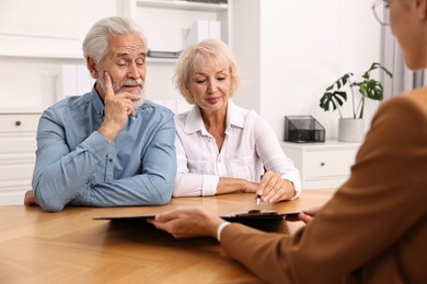 Photo of Pension plan. Senior couple consulting with insurance agent at wooden table indoors