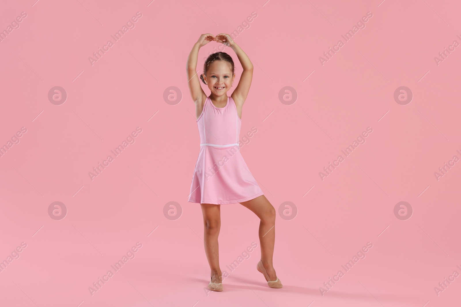 Photo of Little ballerina practicing dance moves on pink background