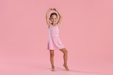 Photo of Little ballerina practicing dance moves on pink background