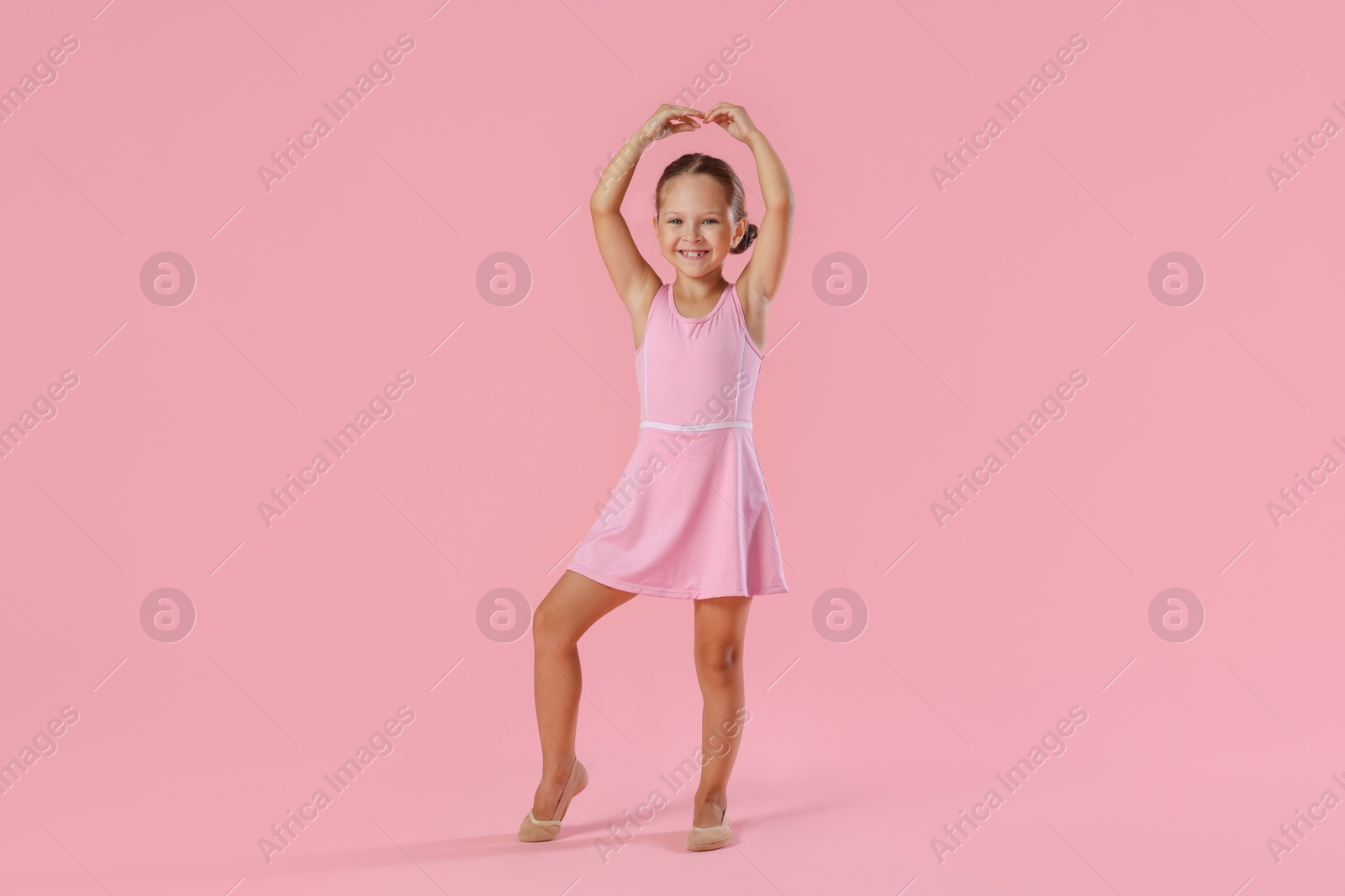 Photo of Little ballerina practicing dance moves on pink background