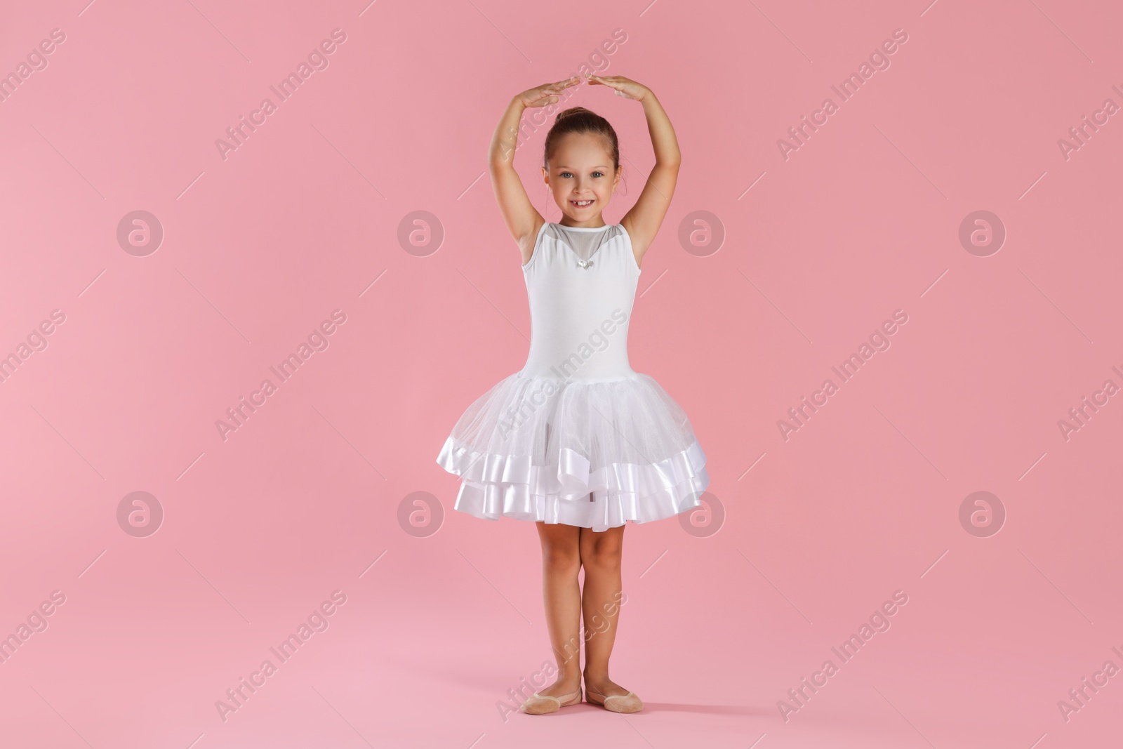 Photo of Little ballerina practicing dance moves on pink background