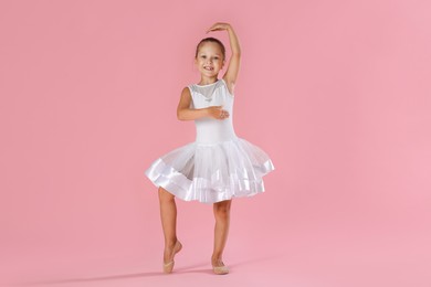 Photo of Little ballerina practicing dance moves on pink background