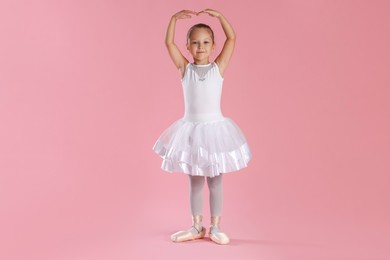 Photo of Little ballerina practicing dance moves on pink background