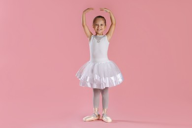 Photo of Little ballerina practicing dance moves on pink background