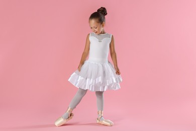 Photo of Little ballerina practicing dance moves on pink background