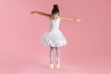 Photo of Little ballerina practicing dance moves on pink background