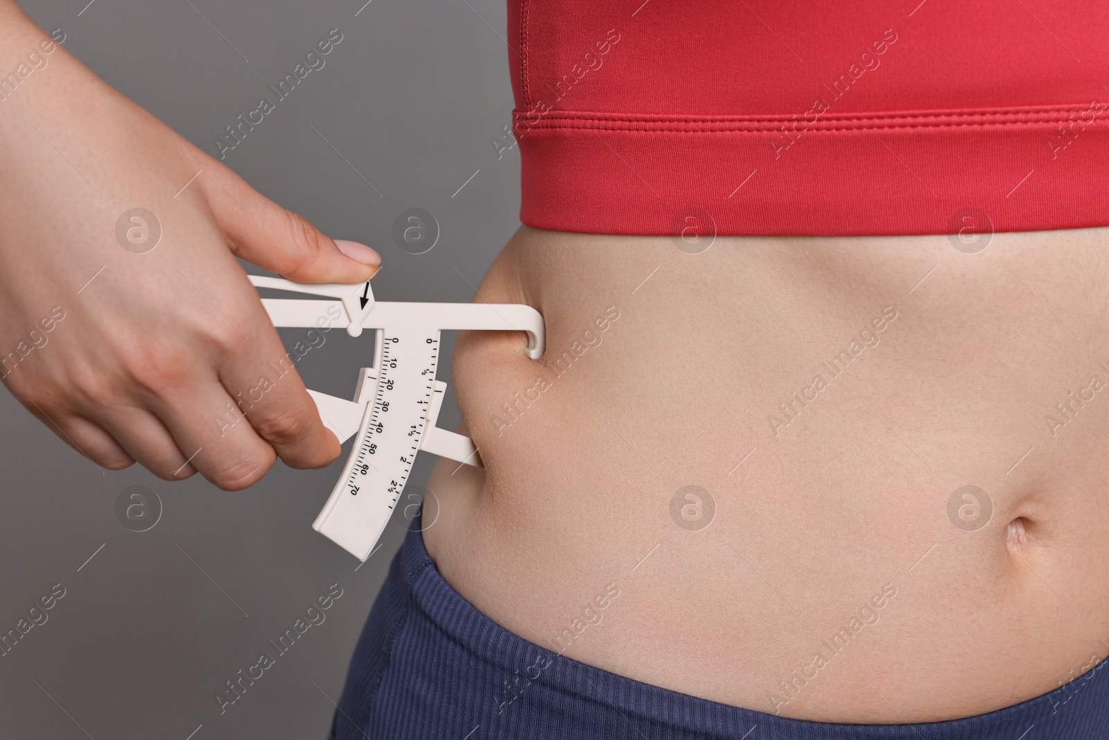 Photo of Woman measuring body fat with caliper on gray background, closeup