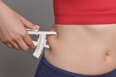 Photo of Woman measuring body fat with caliper on gray background, closeup