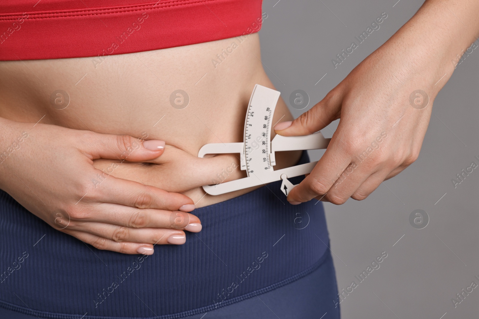 Photo of Woman measuring body fat with caliper on gray background, closeup