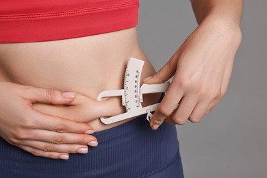 Photo of Woman measuring body fat with caliper on gray background, closeup