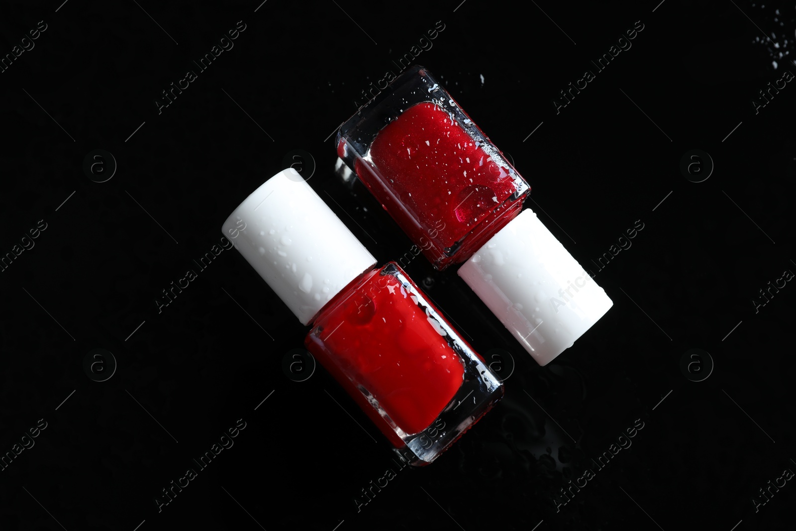 Photo of Nail polishes in bottles on wet dark surface, flat lay