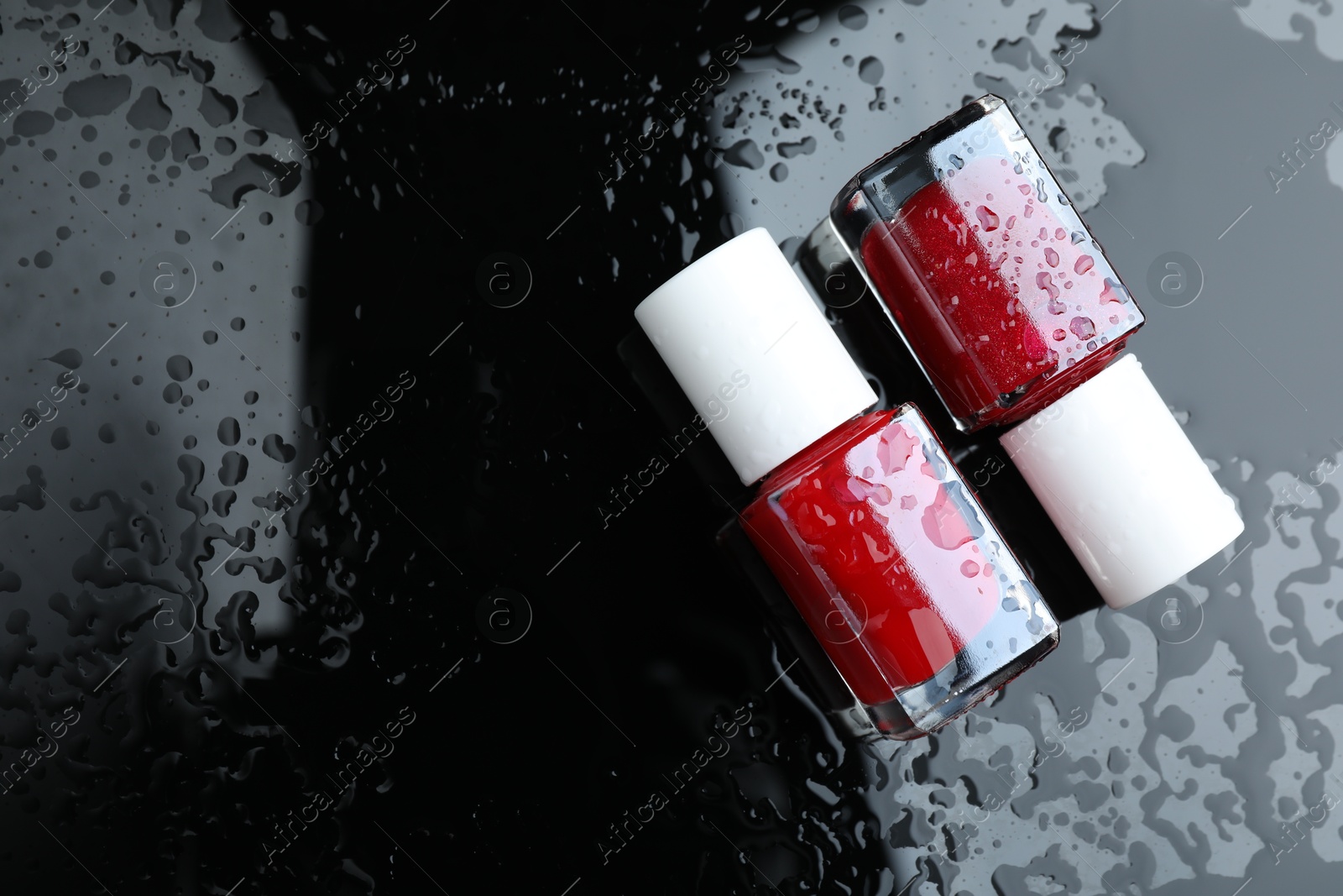 Photo of Nail polishes in bottles on wet dark surface, flat lay. Space for text