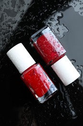 Photo of Nail polishes in bottles on wet dark surface, flat lay