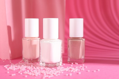 Photo of Nail polishes in bottles and beads on pink background, space for text