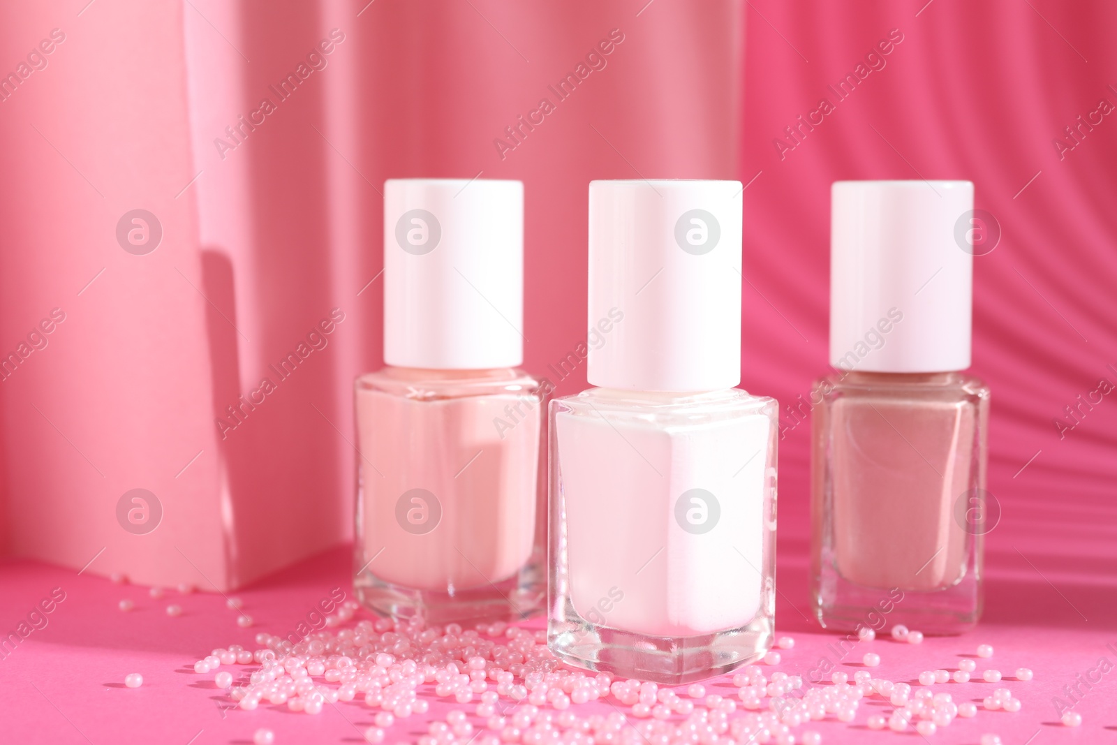 Photo of Nail polishes in bottles and beads on pink background