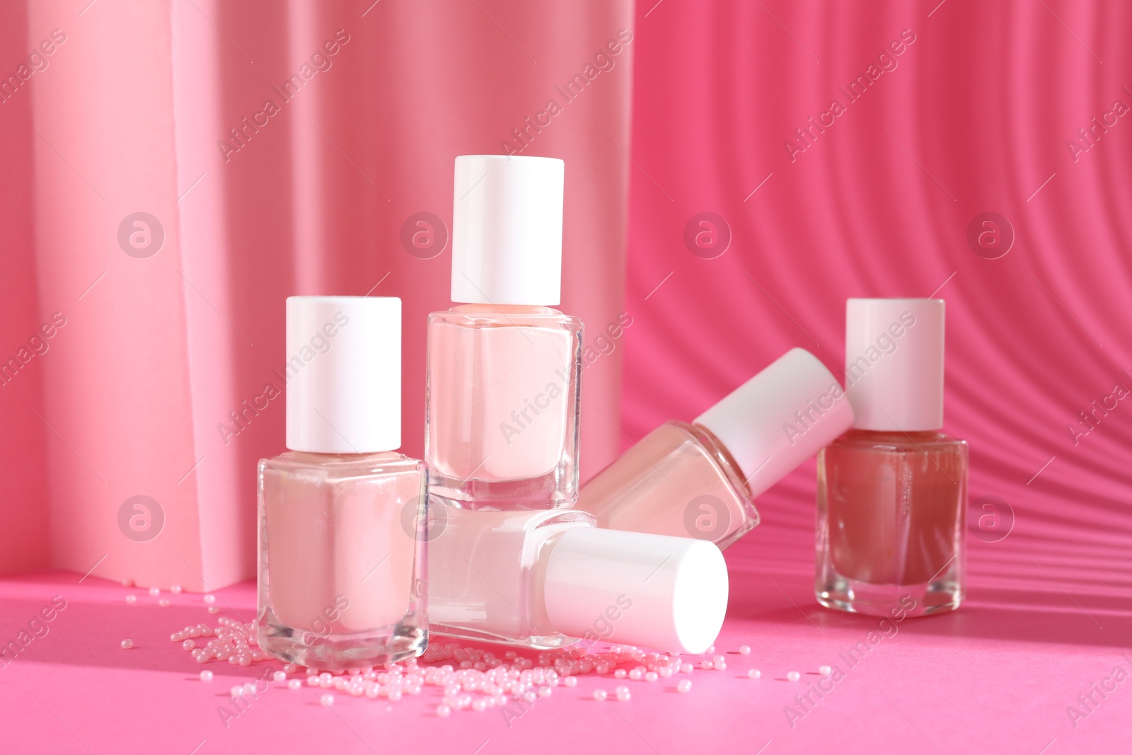 Photo of Nail polishes in bottles and beads on pink background