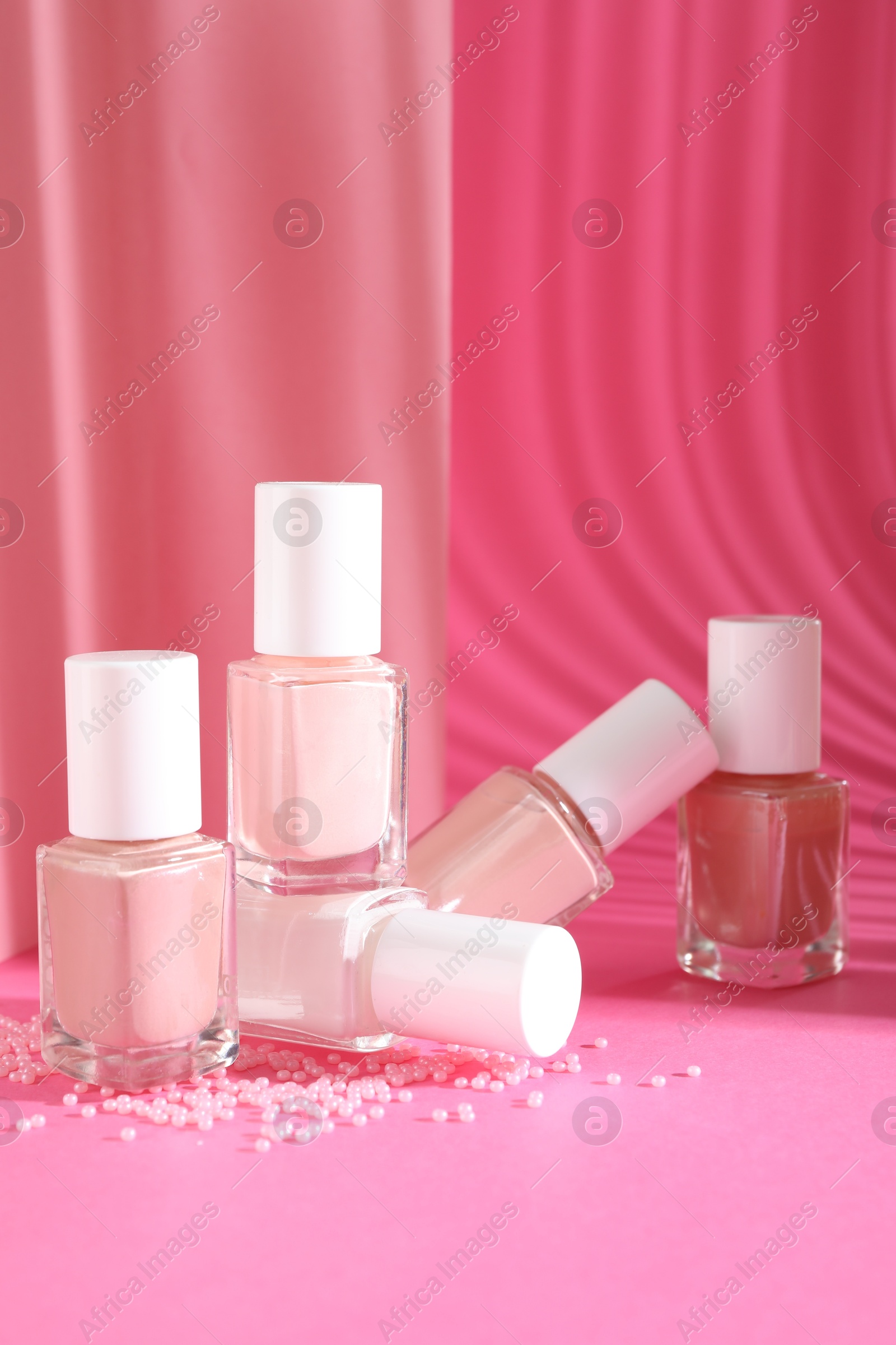 Photo of Nail polishes in bottles and beads on pink background