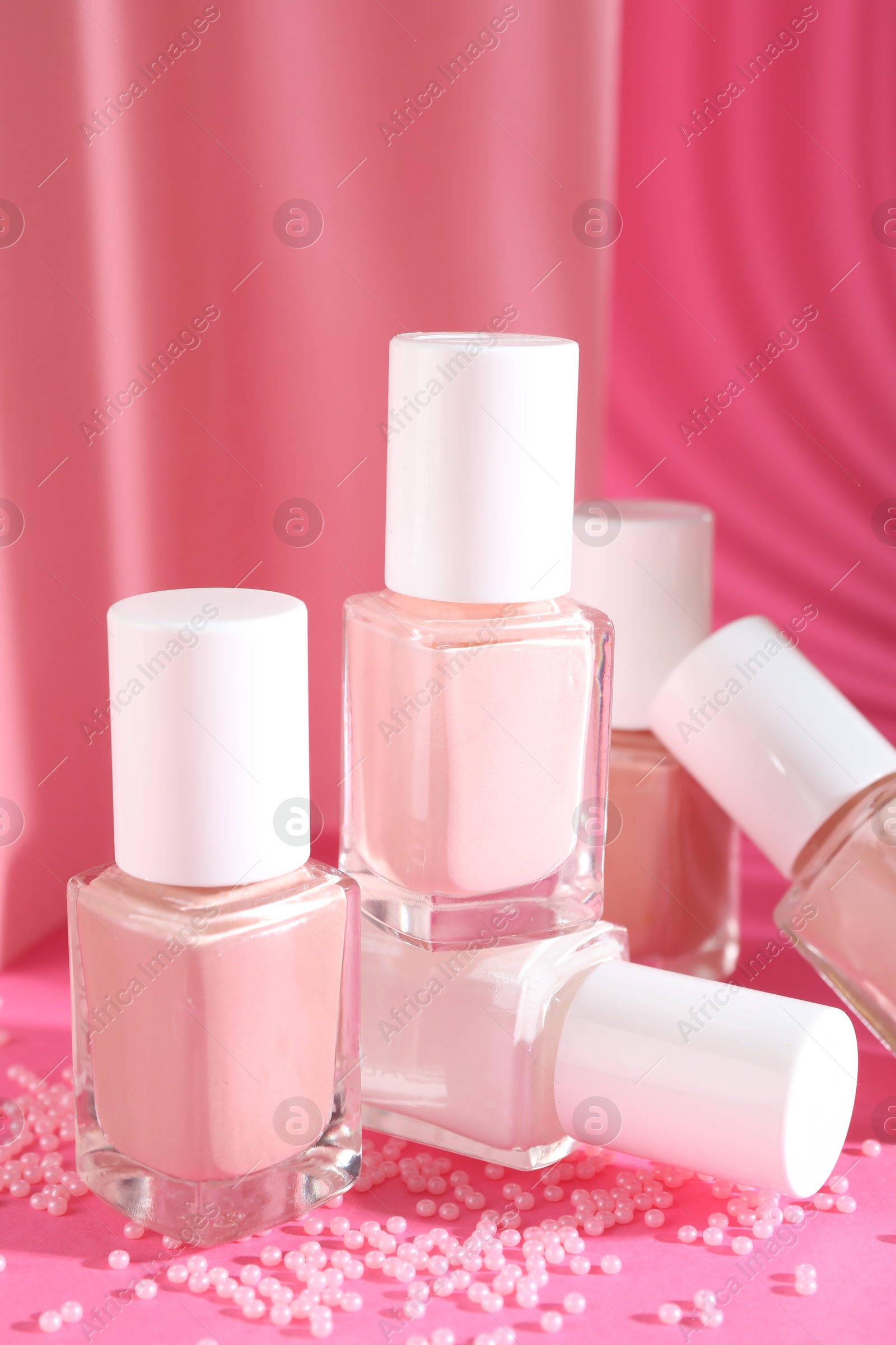 Photo of Nail polishes in bottles and beads on pink background