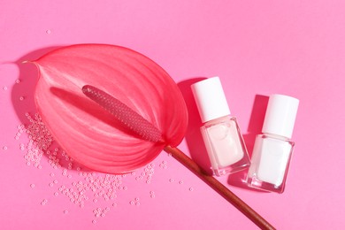 Nail polishes in bottles, beads and tail flower on pink background, flat lay