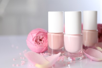 Photo of Nail polishes in bottles, beads and beautiful flowers on white table, closeup. Space for text