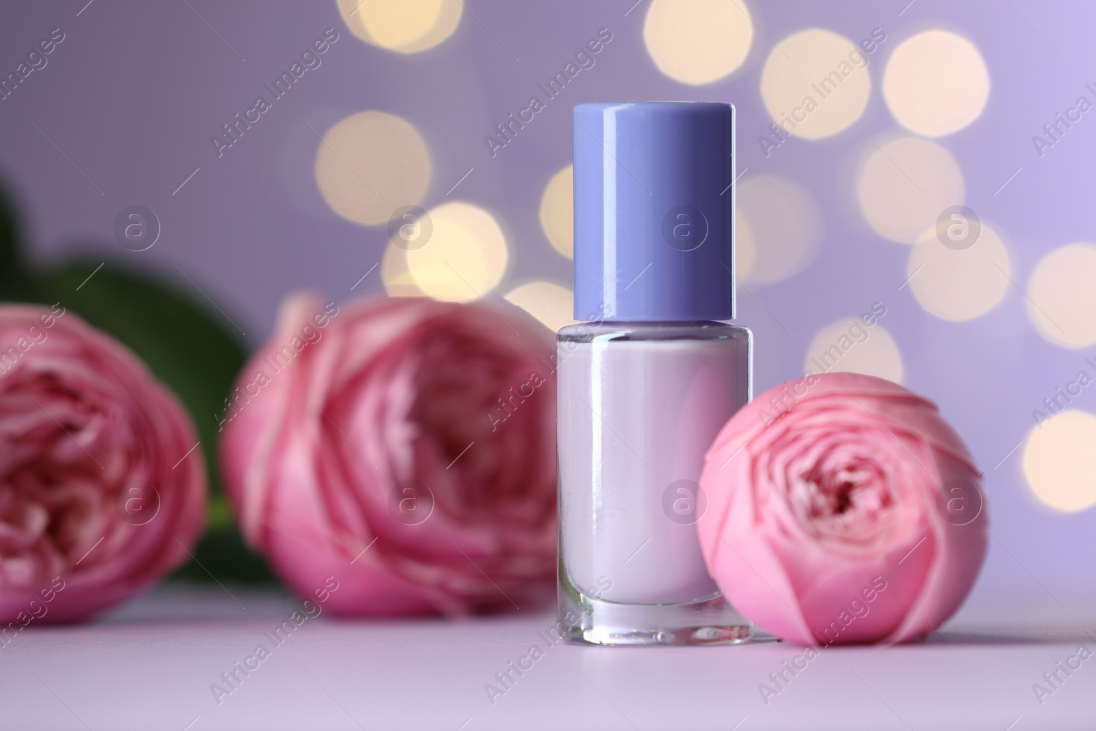 Photo of Nail polish in bottle and beautiful flowers on white table, closeup. Space for text