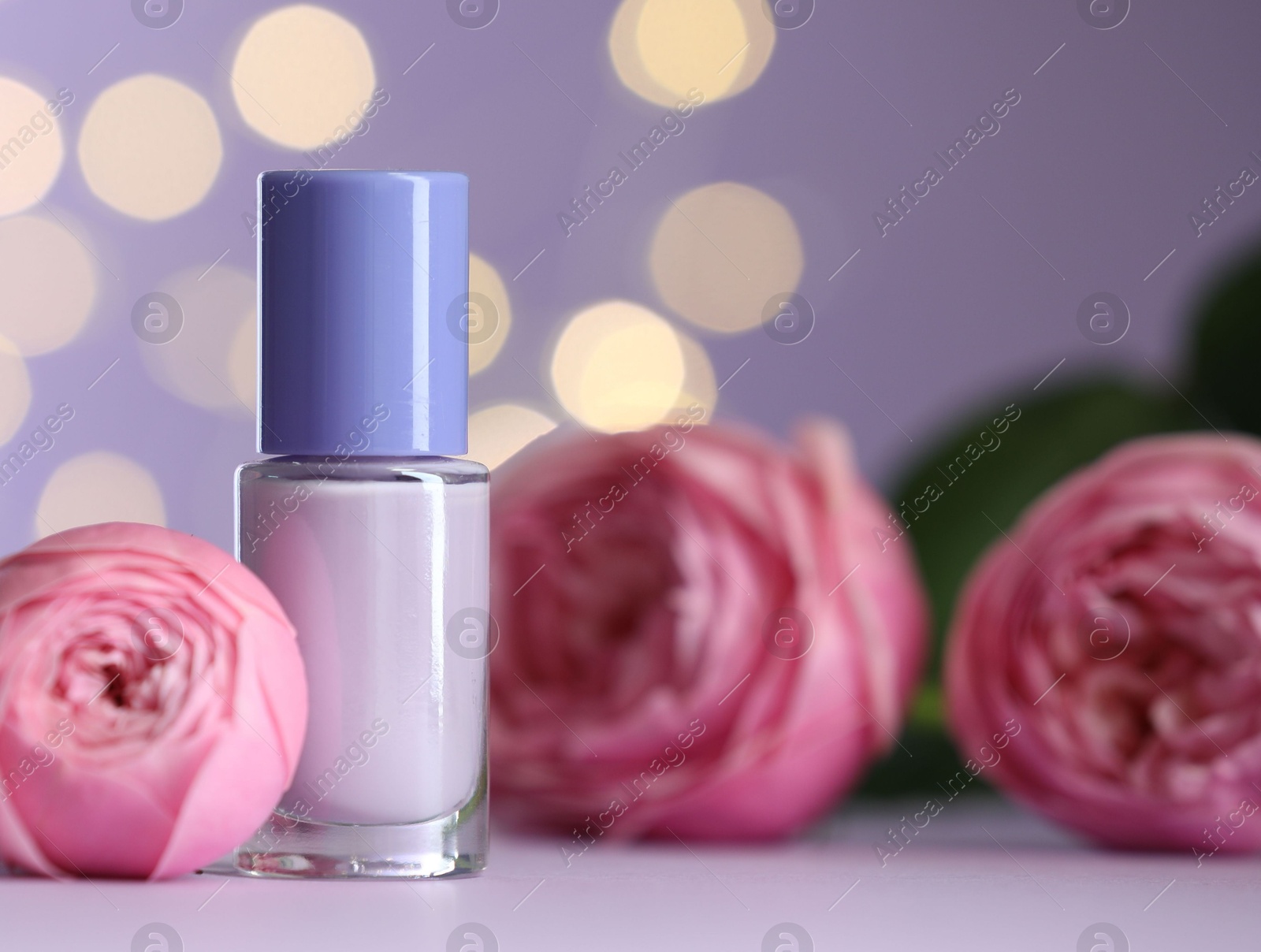 Photo of Nail polish in bottle and beautiful flowers on white table, closeup. Space for text