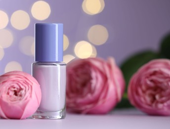 Photo of Nail polish in bottle and beautiful flowers on white table, closeup. Space for text