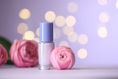 Photo of Nail polish in bottle and beautiful flowers on white table, closeup. Space for text