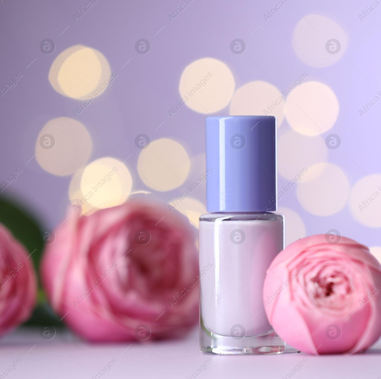 Photo of Nail polish in bottle and beautiful flowers on white table, closeup. Space for text