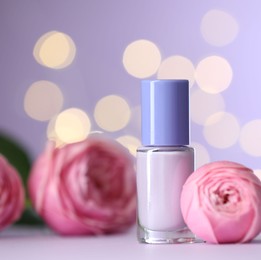 Photo of Nail polish in bottle and beautiful flowers on white table, closeup. Space for text