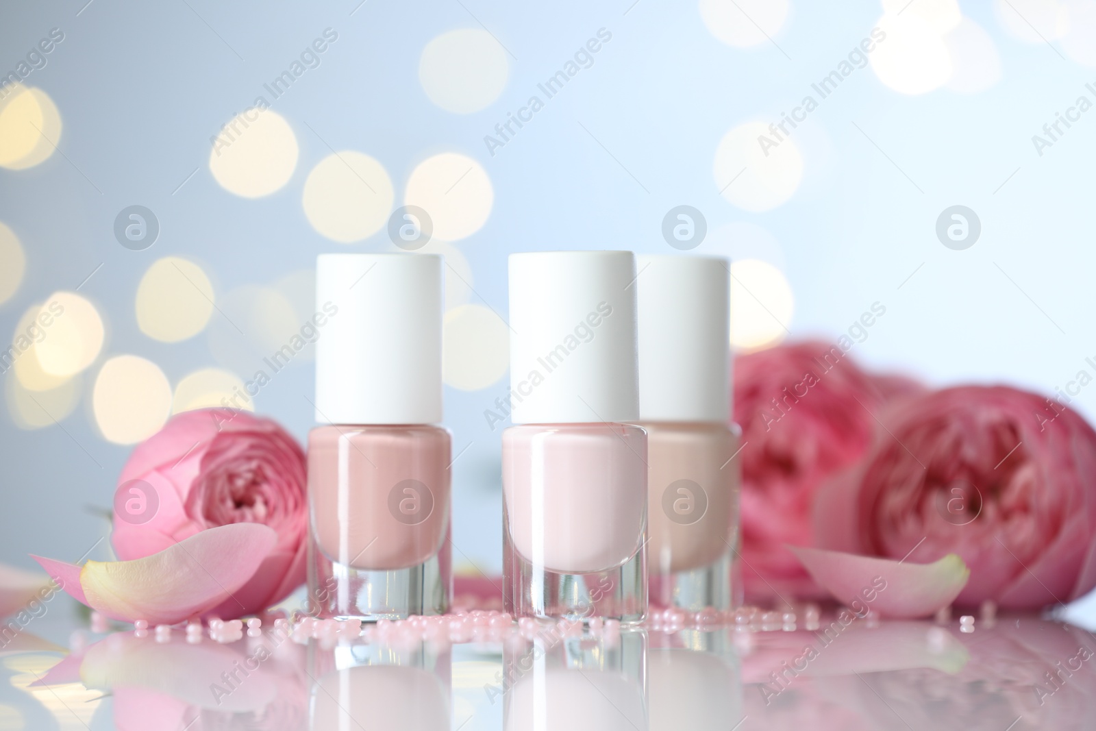 Photo of Nail polishes in bottles, beads and beautiful flowers on white table, closeup