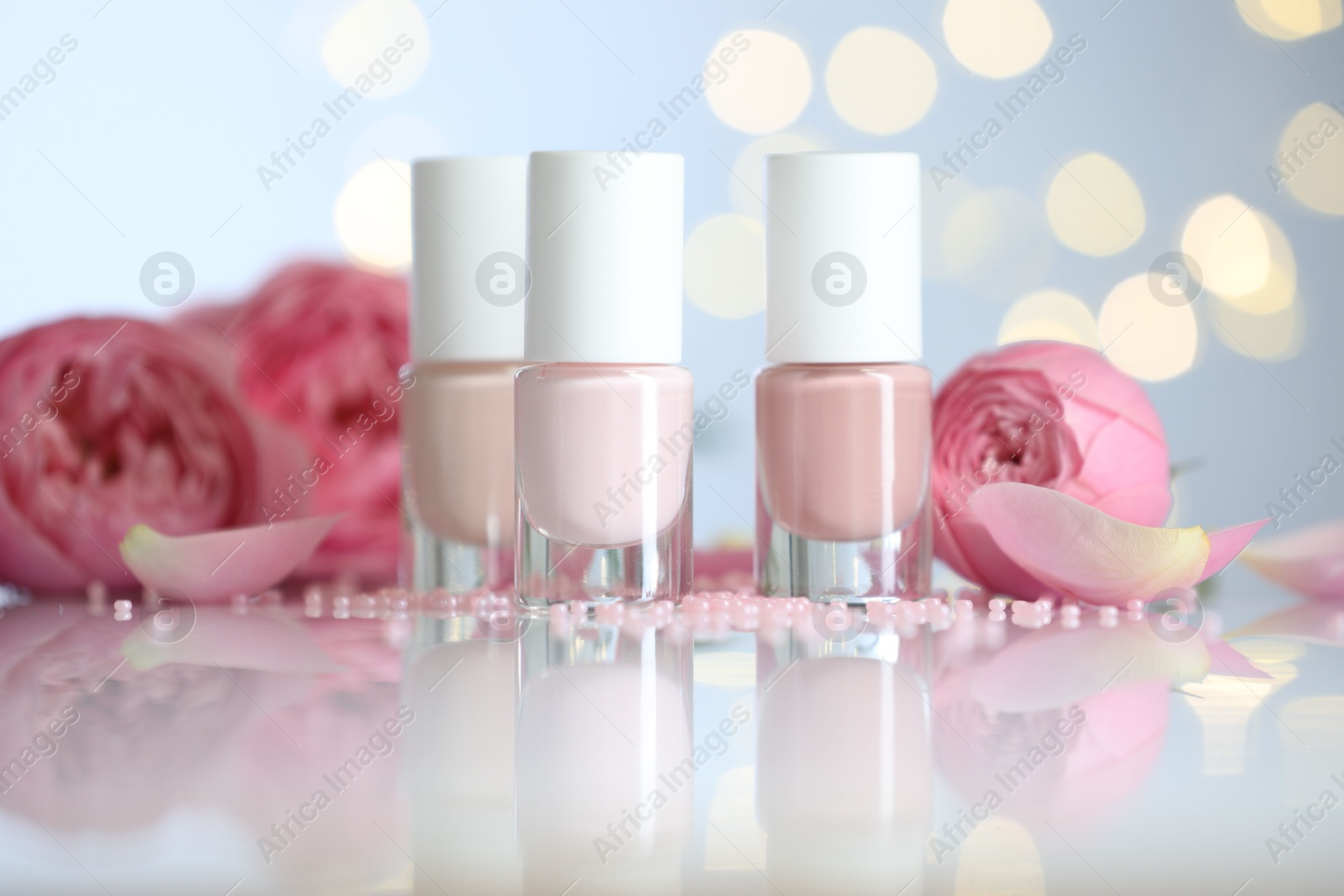 Photo of Nail polishes in bottles, beads and beautiful flowers on white table, closeup