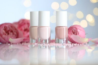 Photo of Nail polishes in bottles, beads and beautiful flowers on white table, closeup