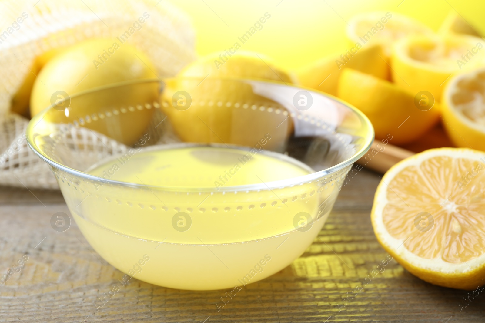 Photo of Bowl with fresh lemon juice and fruits on wooden table, closeup