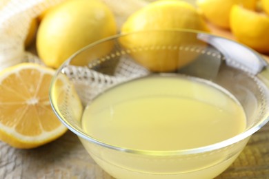 Photo of Bowl with fresh lemon juice and fruits on wooden table, closeup