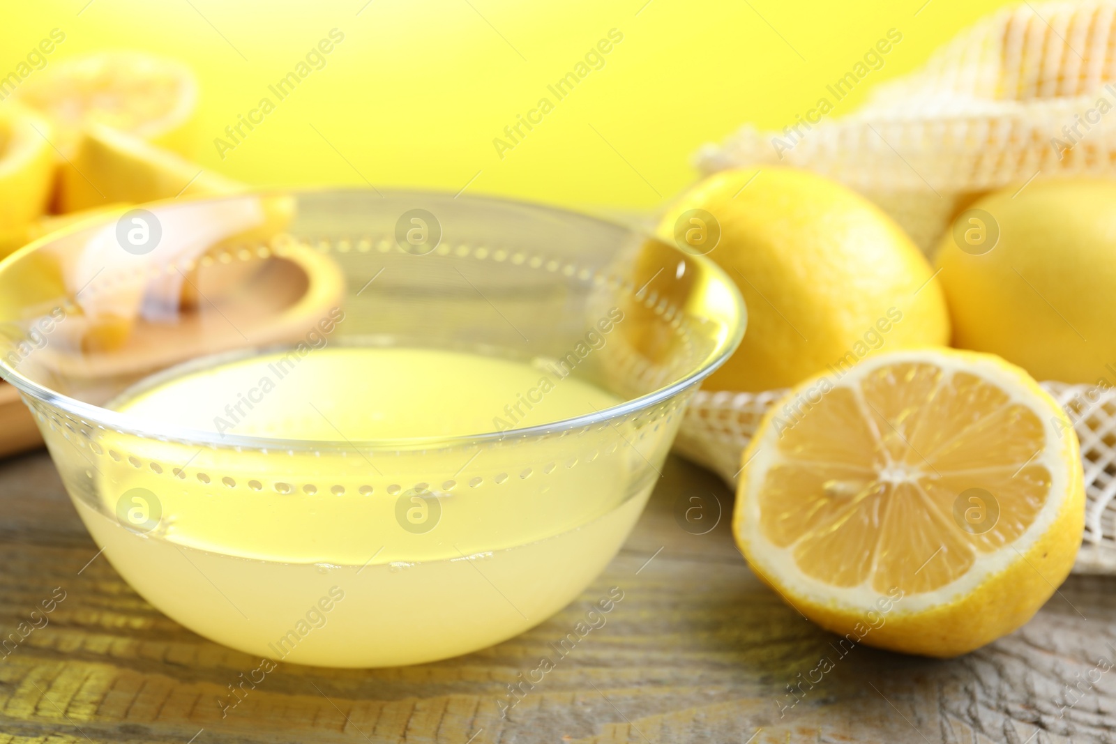 Photo of Bowl with fresh lemon juice and fruits on wooden table, closeup